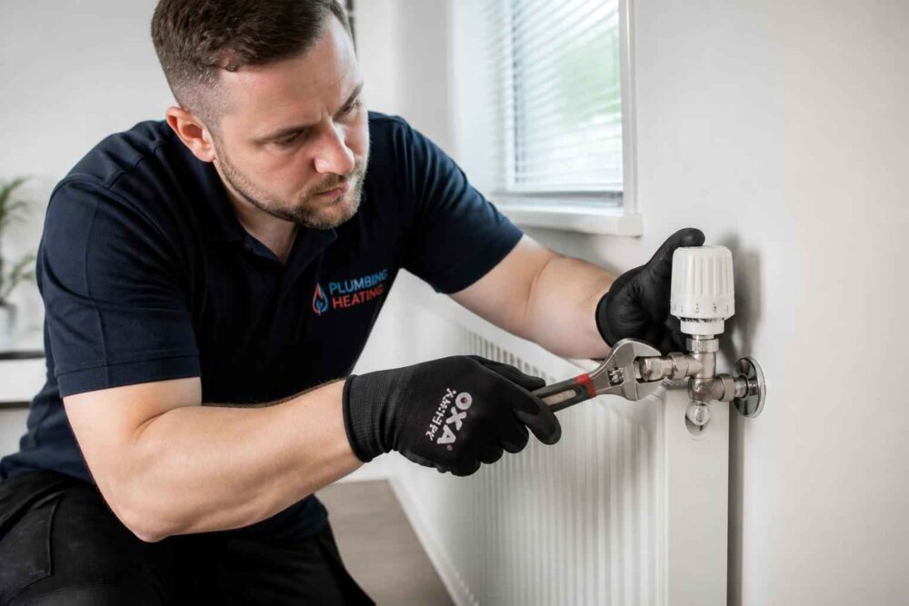 Hydraulik w rękawicach naprawia zawór przy białym grzejniku pokojowym