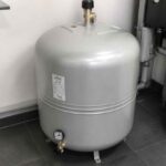 Szary zbiornik ciśnieniowy podłączony do instalacji grzewczej w pomieszczeniu technicznym