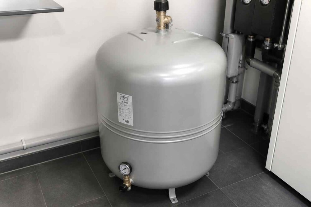 Szary zbiornik ciśnieniowy podłączony do instalacji grzewczej w pomieszczeniu technicznym